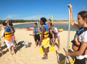 jeunes du séjour jeunes debout sur une plage, avec des gilets de sauvetage, écoutent les instructions avant de partir faire du canoë kayak