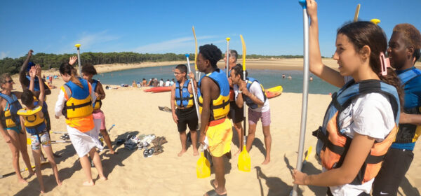 jeunes du séjour jeunes debout sur une plage, avec des gilets de sauvetage, écoutent les instructions avant de partir faire du canoë kayak