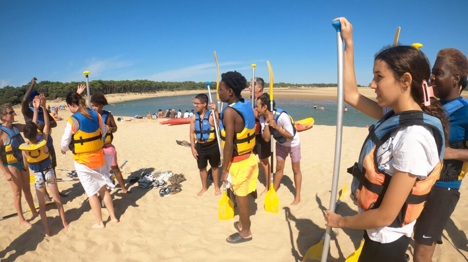 jeunes du séjour jeunes debout sur une plage, avec des gilets de sauvetage, écoutent les instructions avant de partir faire du canoë kayak